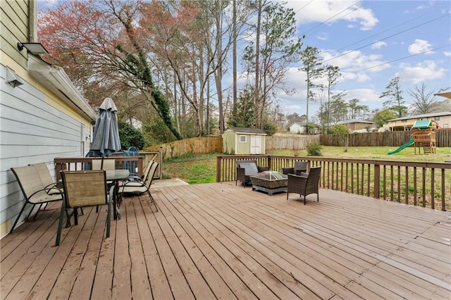 wooden terrace featuring a fenced backyard, a yard, outdoor dining area, a shed, and a playground