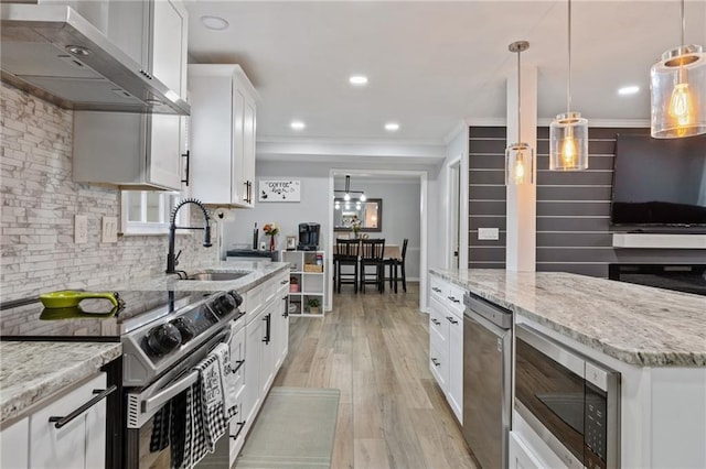 kitchen featuring light wood-style floors, appliances with stainless steel finishes, wall chimney range hood, backsplash, and a sink