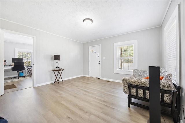 sitting room with baseboards, a textured ceiling, wood finished floors, and crown molding