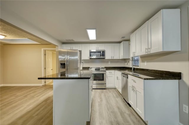 kitchen with light wood-type flooring, stainless steel appliances, sink, white cabinets, and a kitchen island