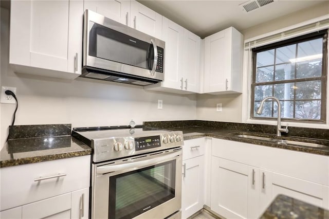 kitchen with stainless steel appliances, white cabinetry, dark stone counters, and sink