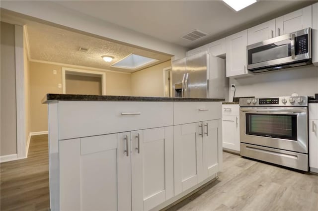 kitchen with light hardwood / wood-style flooring, dark stone countertops, a textured ceiling, appliances with stainless steel finishes, and white cabinetry