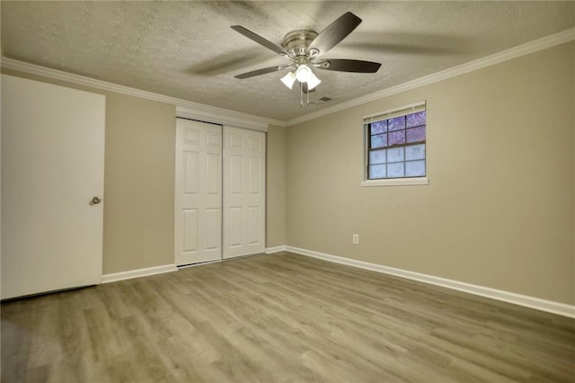 unfurnished bedroom featuring ceiling fan, hardwood / wood-style floors, a textured ceiling, a closet, and ornamental molding