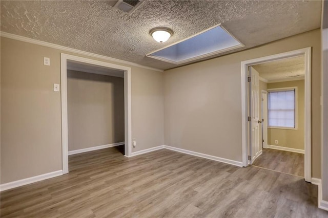 empty room with a textured ceiling, light hardwood / wood-style flooring, and crown molding