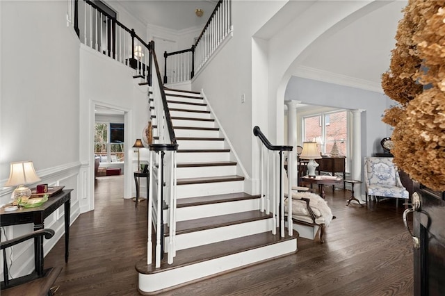 staircase featuring arched walkways, wood finished floors, plenty of natural light, and decorative columns