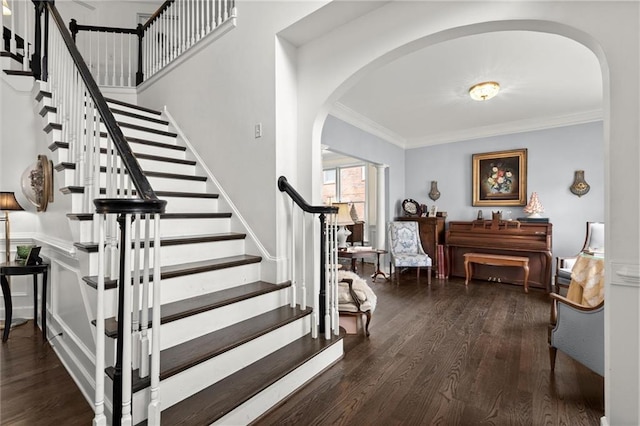 foyer with arched walkways, wood finished floors, and crown molding