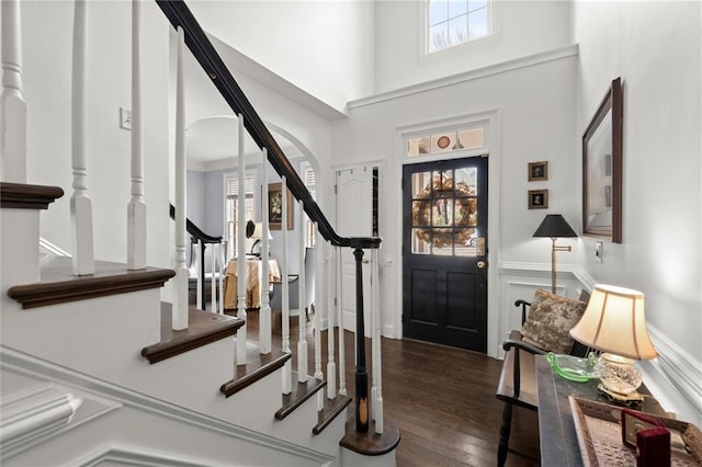 entrance foyer with arched walkways, wainscoting, wood finished floors, stairs, and a high ceiling