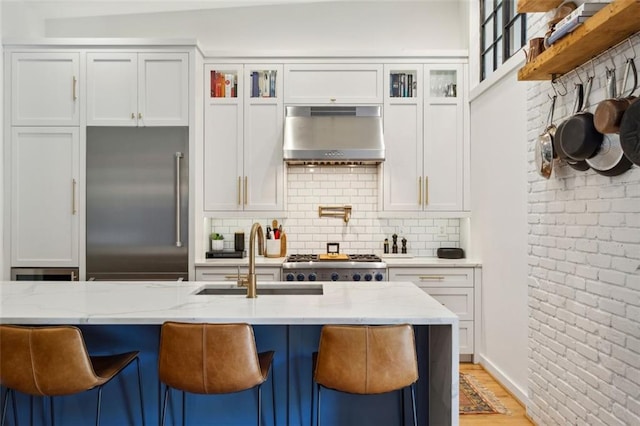 kitchen with under cabinet range hood, a sink, light stone countertops, and built in fridge