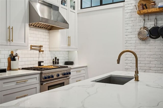 kitchen with backsplash, high end stove, exhaust hood, white cabinetry, and a sink