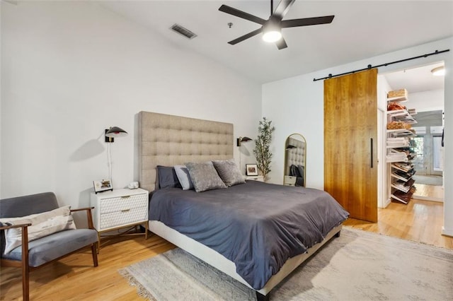 bedroom with visible vents, a walk in closet, light wood-type flooring, a barn door, and a ceiling fan