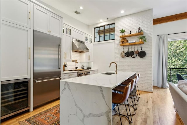 kitchen featuring visible vents, a sink, wine cooler, under cabinet range hood, and built in refrigerator