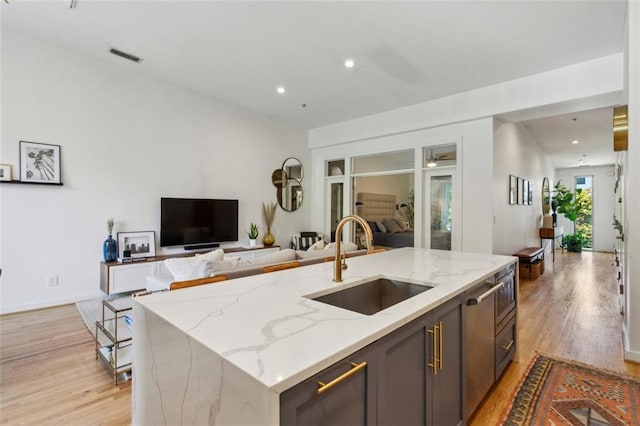 kitchen featuring visible vents, light wood-style flooring, light stone countertops, and a sink