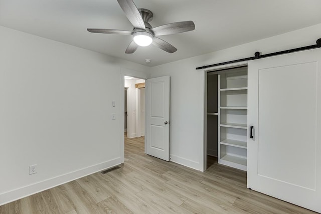 unfurnished bedroom with a barn door, ceiling fan, a closet, and light wood-type flooring