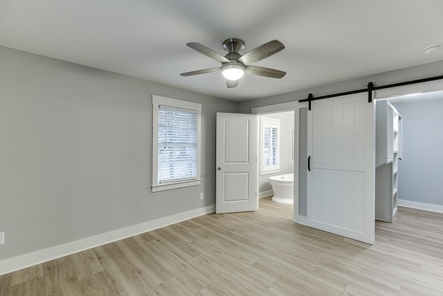 unfurnished bedroom with a barn door, ensuite bathroom, ceiling fan, and light wood-type flooring