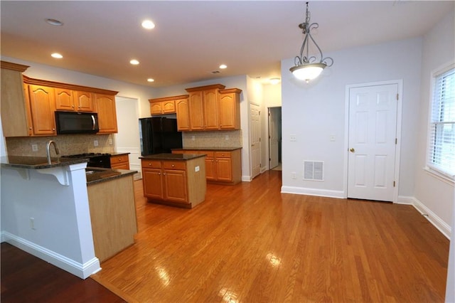 kitchen featuring a kitchen island, black refrigerator, dark hardwood / wood-style floors, decorative backsplash, and hanging light fixtures