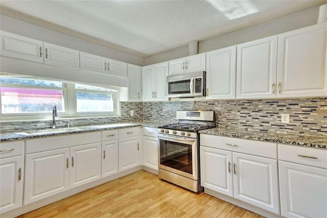 kitchen featuring tasteful backsplash, stainless steel appliances, sink, light hardwood / wood-style flooring, and white cabinets