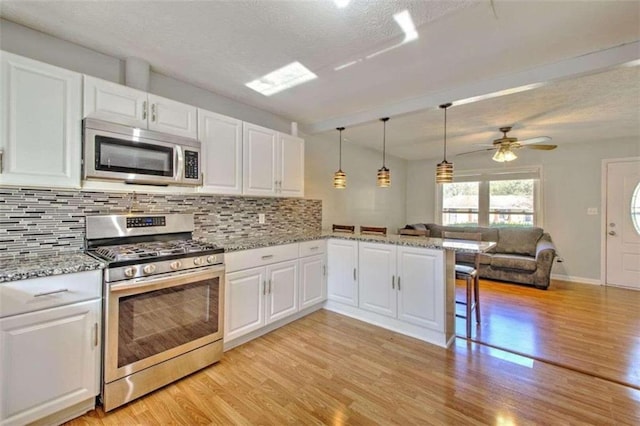 kitchen featuring kitchen peninsula, white cabinetry, stainless steel appliances, and decorative light fixtures