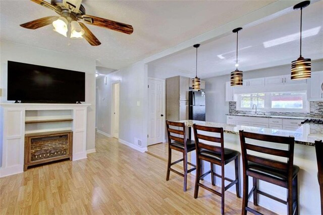 kitchen with a kitchen breakfast bar, tasteful backsplash, black fridge, light hardwood / wood-style floors, and white cabinetry