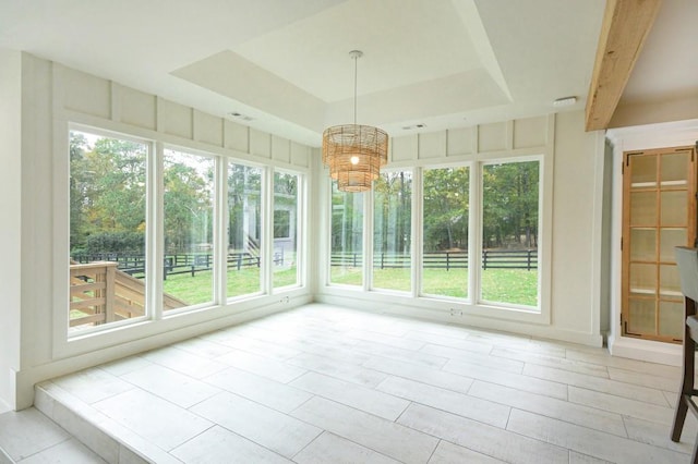 unfurnished sunroom featuring a chandelier, a tray ceiling, and a healthy amount of sunlight