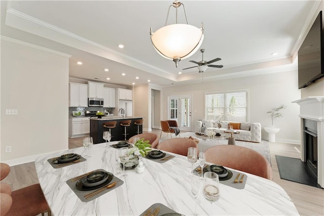 dining room featuring ceiling fan, sink, light hardwood / wood-style flooring, crown molding, and a tray ceiling