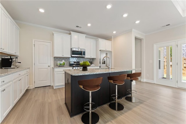 kitchen with sink, ornamental molding, a center island with sink, white cabinets, and appliances with stainless steel finishes