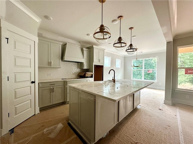 7040 Manchester Dr, Flowery Branch, GA 30542 - kitchen with custom exhaust hood, a kitchen island with sink, decorative backsplash, ornamental molding, and light stone countertops