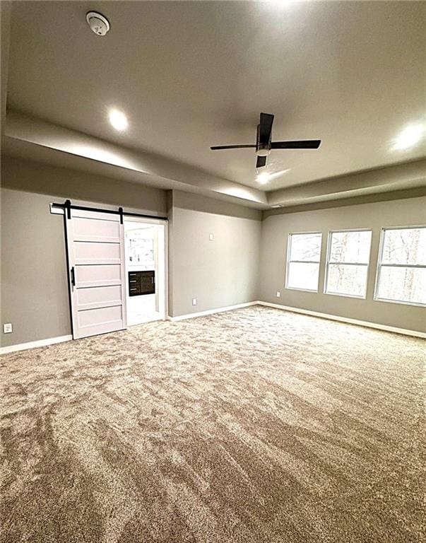 unfurnished living room featuring ceiling fan, carpet flooring, and a barn door