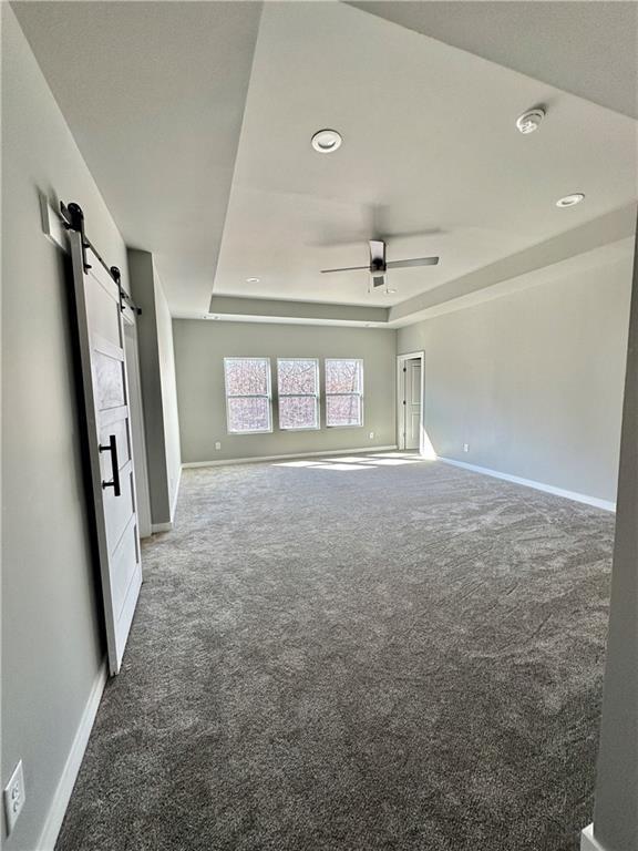 carpeted empty room with a tray ceiling, a barn door, and ceiling fan