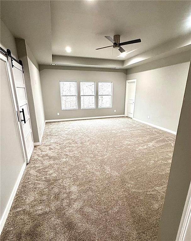 carpeted spare room with a tray ceiling, a barn door, and ceiling fan