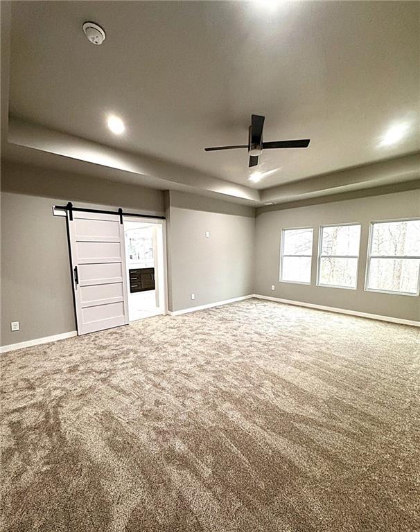 unfurnished living room with carpet floors, a barn door, and ceiling fan