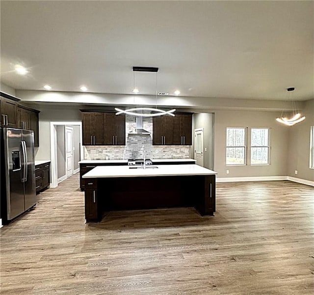 kitchen with pendant lighting, sink, stainless steel fridge with ice dispenser, dark brown cabinets, and a center island with sink