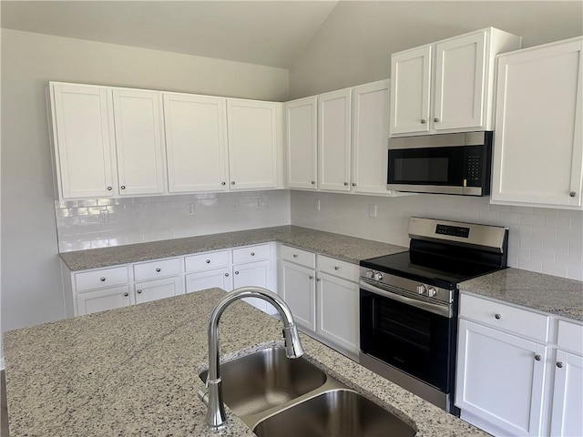 kitchen with tasteful backsplash, white cabinets, lofted ceiling, stainless steel appliances, and a sink