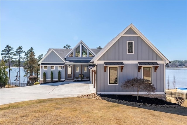 modern inspired farmhouse featuring a shingled roof, concrete driveway, a water view, board and batten siding, and a front yard