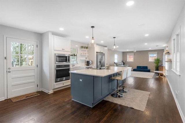 kitchen with appliances with stainless steel finishes, decorative light fixtures, white cabinetry, sink, and a center island with sink