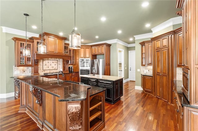 kitchen featuring sink, hanging light fixtures, appliances with stainless steel finishes, an island with sink, and dark stone counters