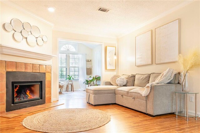 living room with a fireplace, ornamental molding, light wood-type flooring, and a textured ceiling