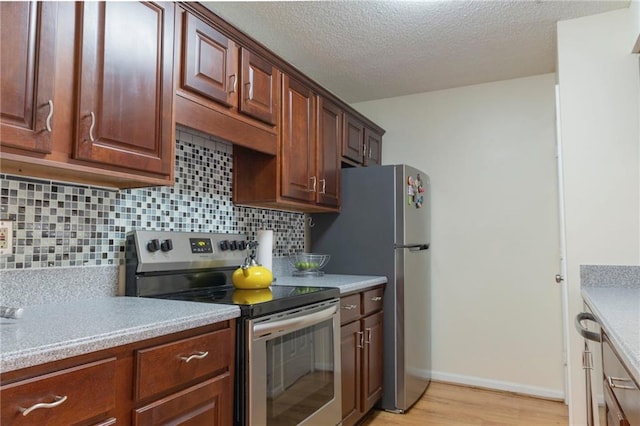 kitchen featuring light wood finished floors, decorative backsplash, stainless steel appliances, a textured ceiling, and light countertops