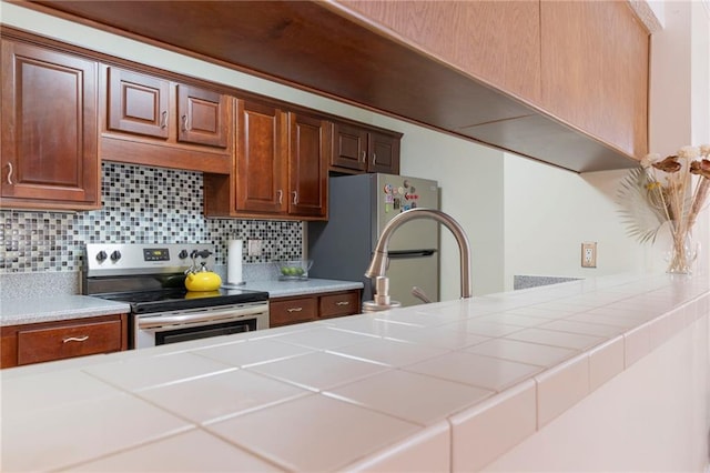 kitchen with brown cabinets, appliances with stainless steel finishes, tile counters, and decorative backsplash