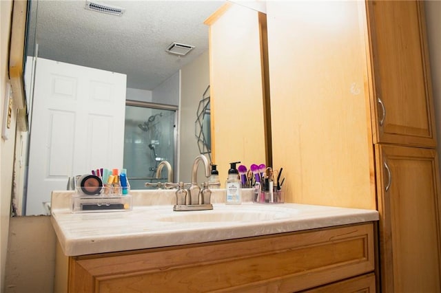 full bath featuring visible vents, a shower with door, a textured ceiling, and vanity