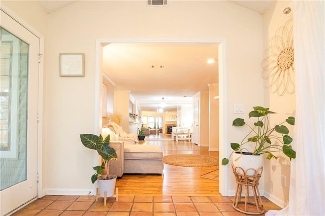 hallway featuring lofted ceiling, visible vents, baseboards, and light tile patterned flooring