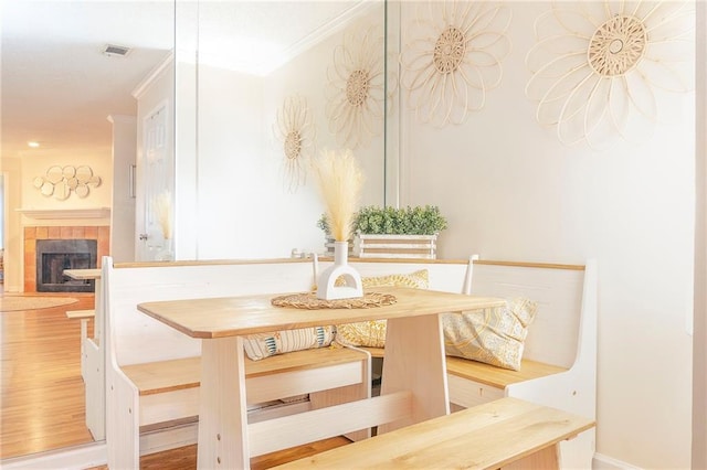 dining space with a tile fireplace, visible vents, crown molding, and wood finished floors