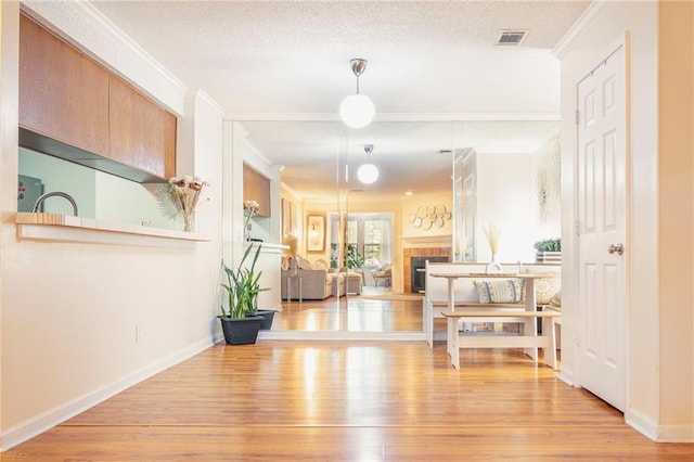 hall featuring light wood-type flooring, a textured ceiling, baseboards, and crown molding