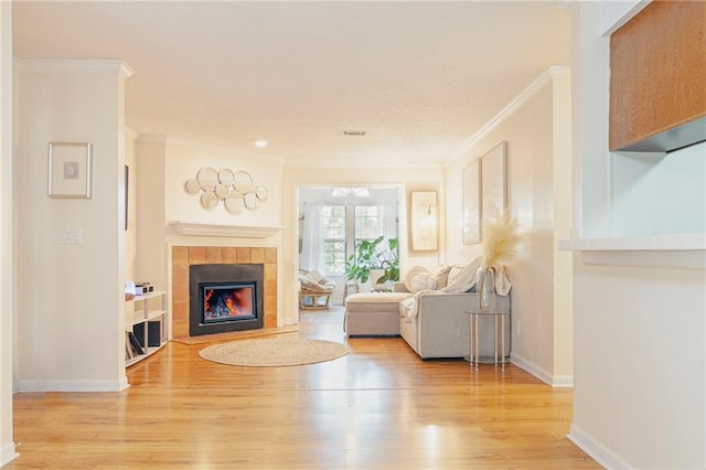 living area with light wood-type flooring, crown molding, baseboards, and a tiled fireplace