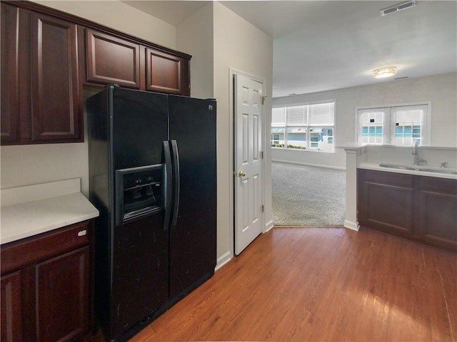 kitchen with black fridge with ice dispenser, dark brown cabinetry, sink, and light colored carpet