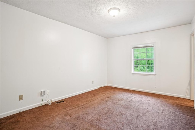 empty room with carpet flooring, visible vents, a textured ceiling, and baseboards
