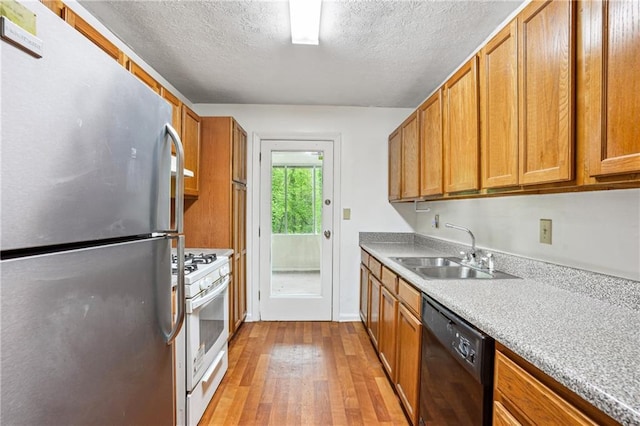 kitchen with freestanding refrigerator, white gas range, dishwasher, a sink, and light wood finished floors