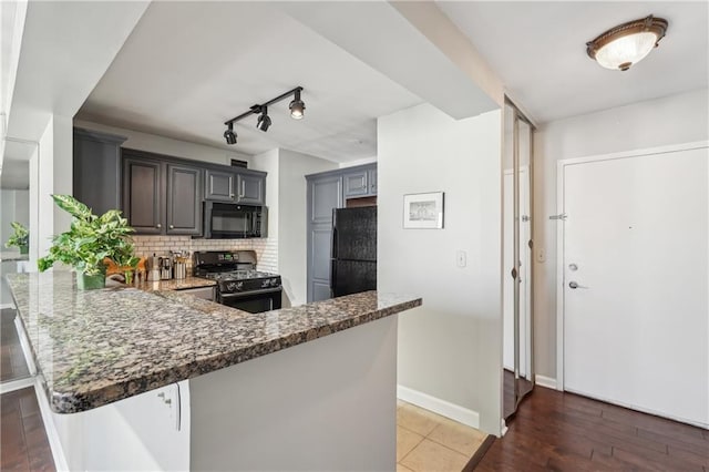 kitchen featuring dark stone countertops, black appliances, rail lighting, and kitchen peninsula