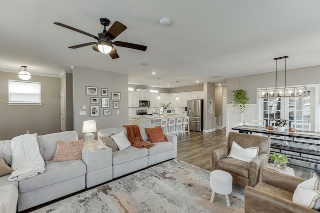 living room featuring crown molding, hardwood / wood-style floors, ceiling fan with notable chandelier, and sink