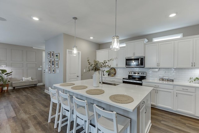 kitchen featuring appliances with stainless steel finishes, white cabinetry, an island with sink, sink, and hanging light fixtures