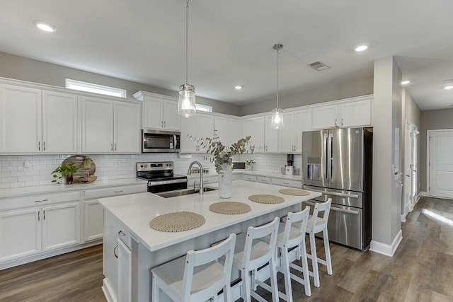 kitchen with pendant lighting, sink, white cabinetry, stainless steel appliances, and a center island with sink